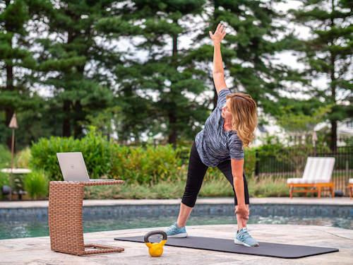 Woman excercising virtually with her laptop near a pool