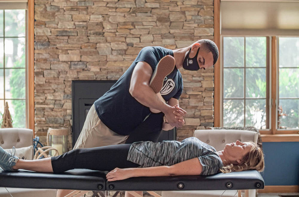 Personal trainer helping older woman stretch in-home